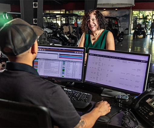 Man sitting in front of two computer monitors helping a woman in a dealership