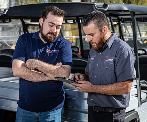 Two men looking at a tablet in front of parked golf carts