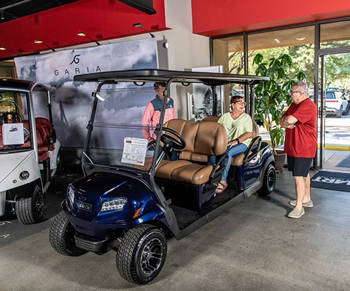 A man and woman discussing a golf cart with a salesperson inside of a building