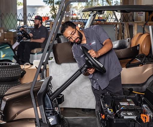 Two workers inspecting and maintaining golf carts