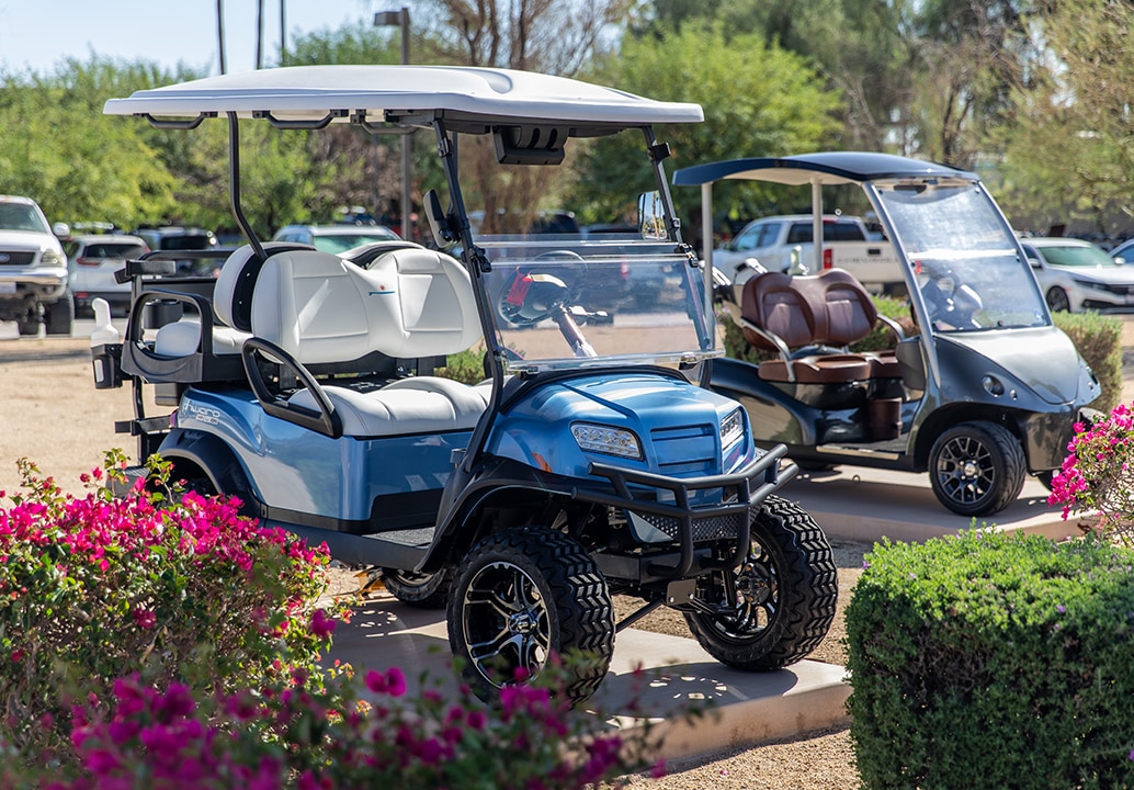 Two blue golf carts parked in a parking lot with cars