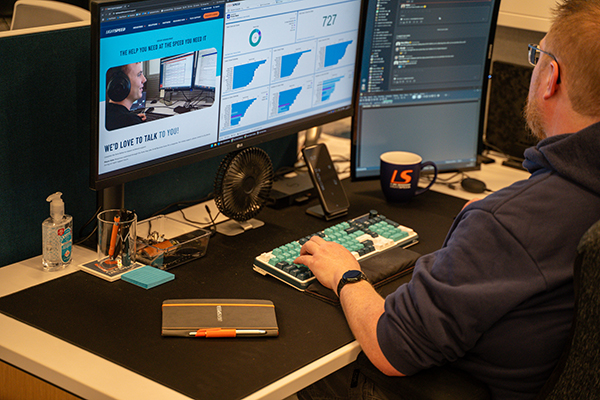 A man at a desk looking at a screen with statistics and a scree of the Lightspeed website on his computer.