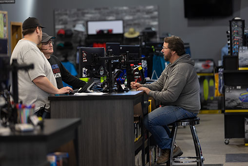 Image of three men talking around a computer monitor at a desk.